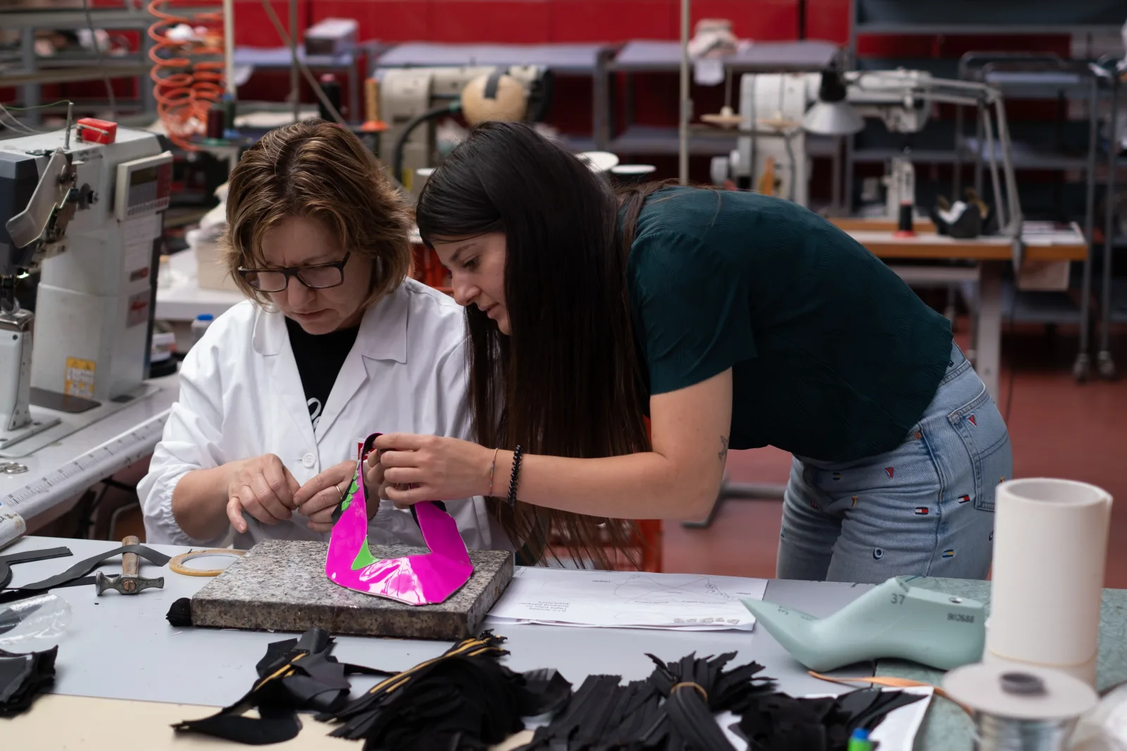 Susanna Zampieri in fabbrica con un'artigiana mentre lavorano un prototipo di scarpa rosa al banco con macchine da cucire industriali